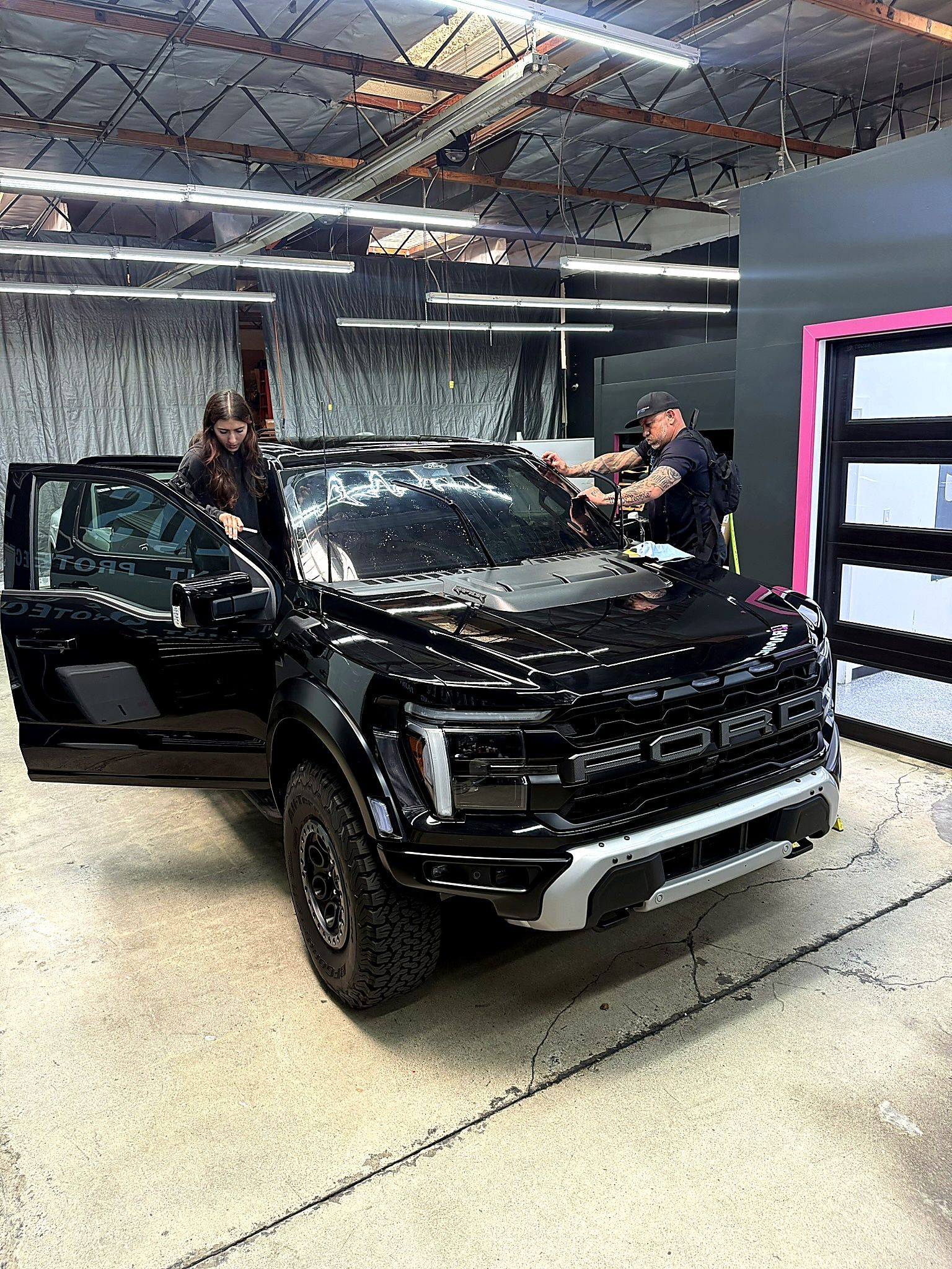 Black SUV in a garage, with two people inspecting it under bright overhead lights.