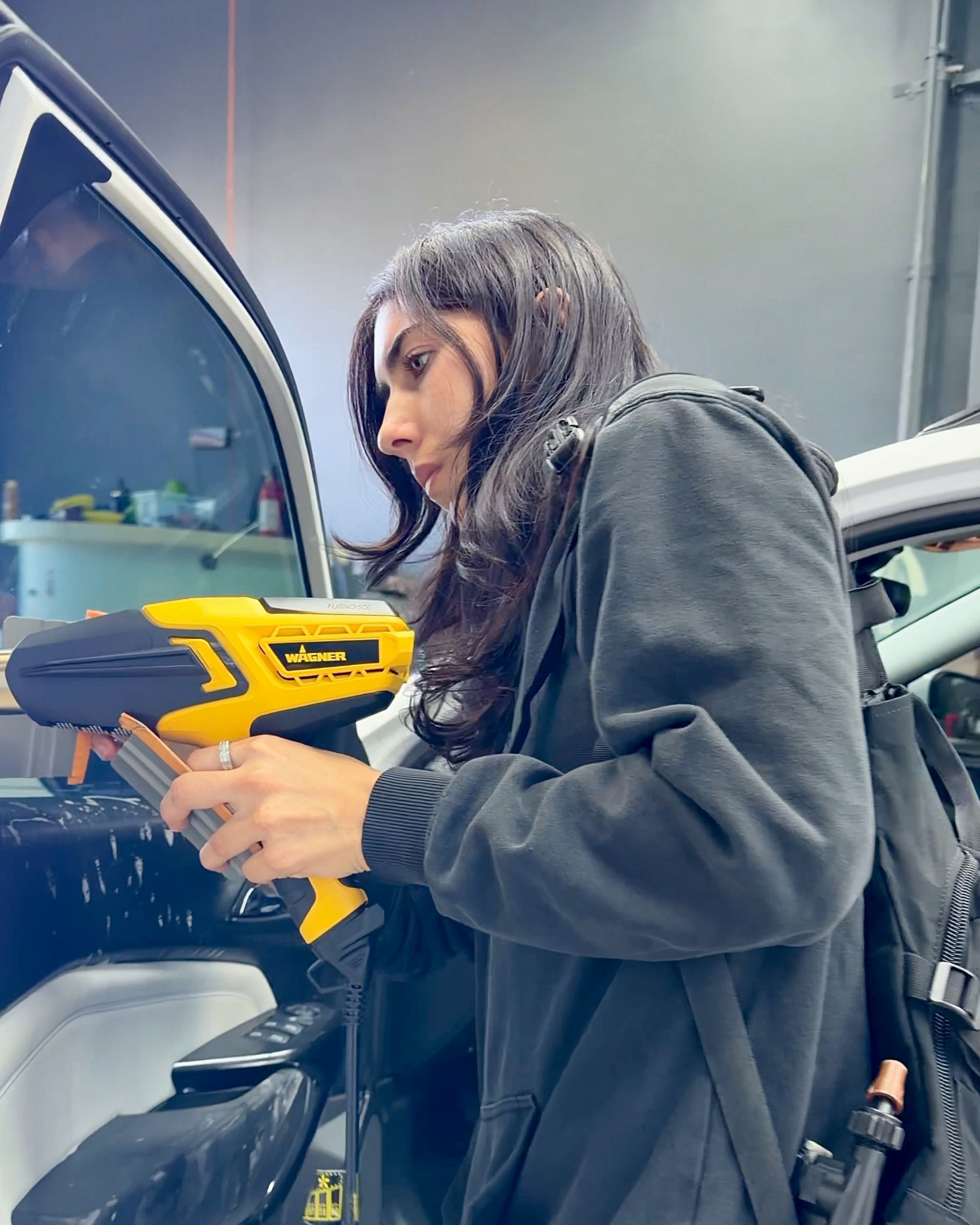 Person using a yellow power drill on a car door in a workshop
