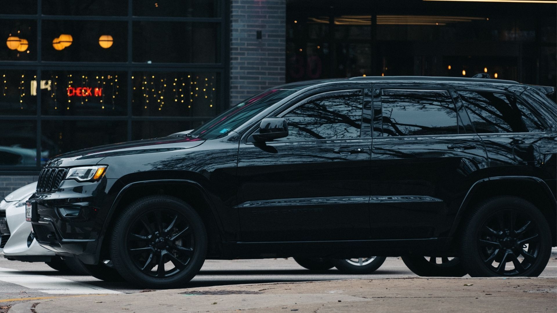 Black SUV parked on a wet city street in front of lit storefront windows