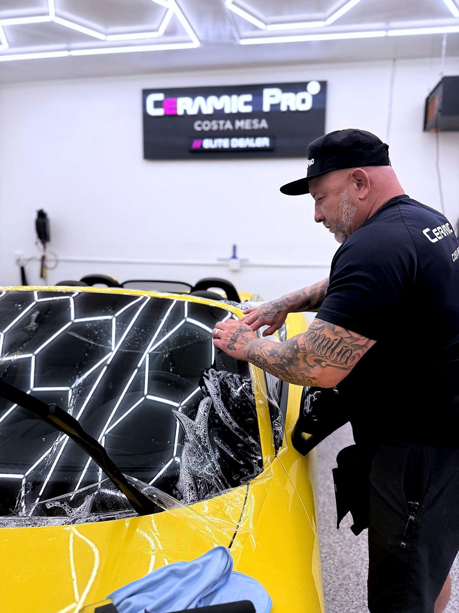 Technician applying protective film to a yellow sports car at Ceramic Pro Costa Mesa.