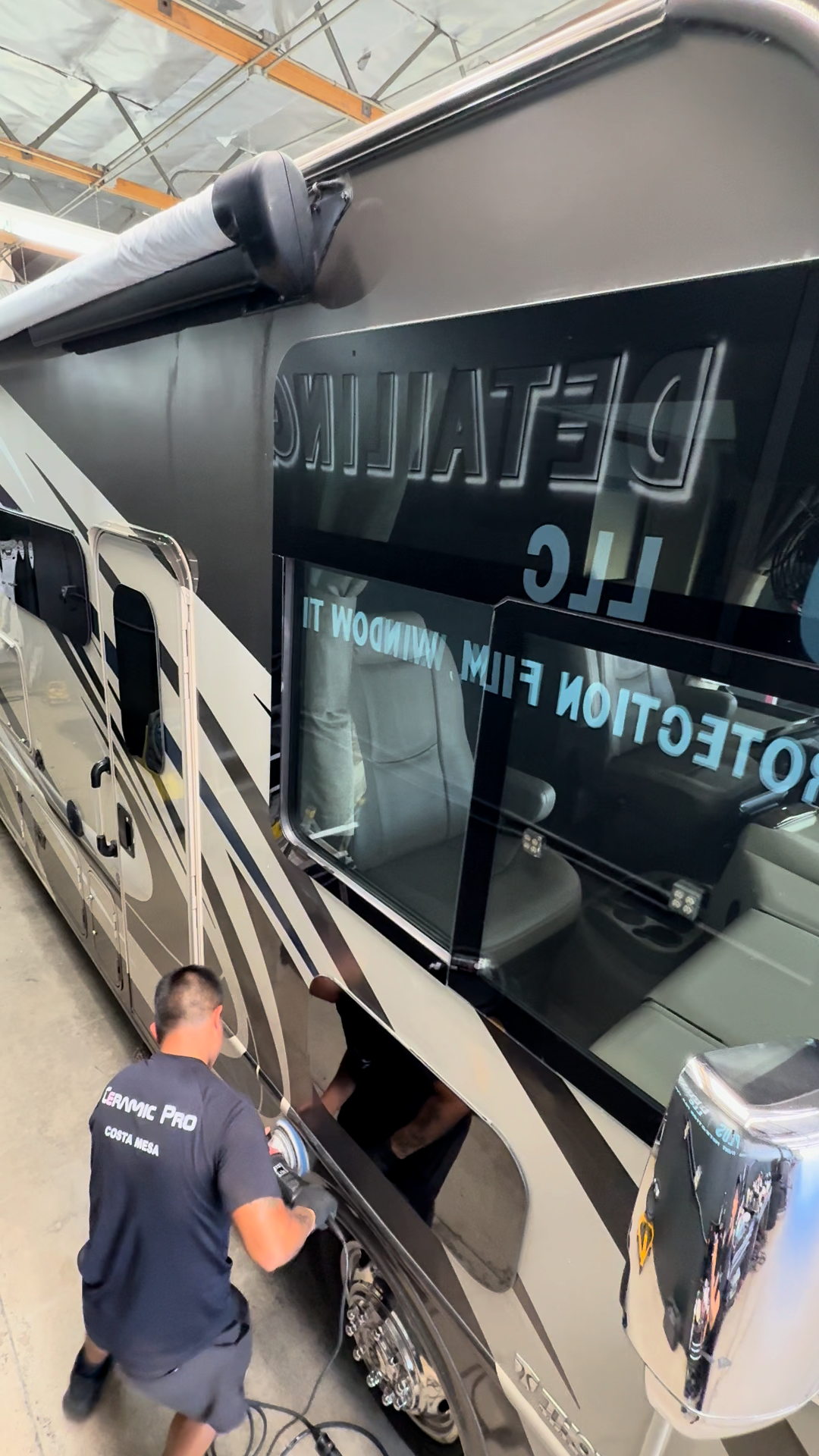 Person cleaning the side of a black and silver tour bus with reflective windows