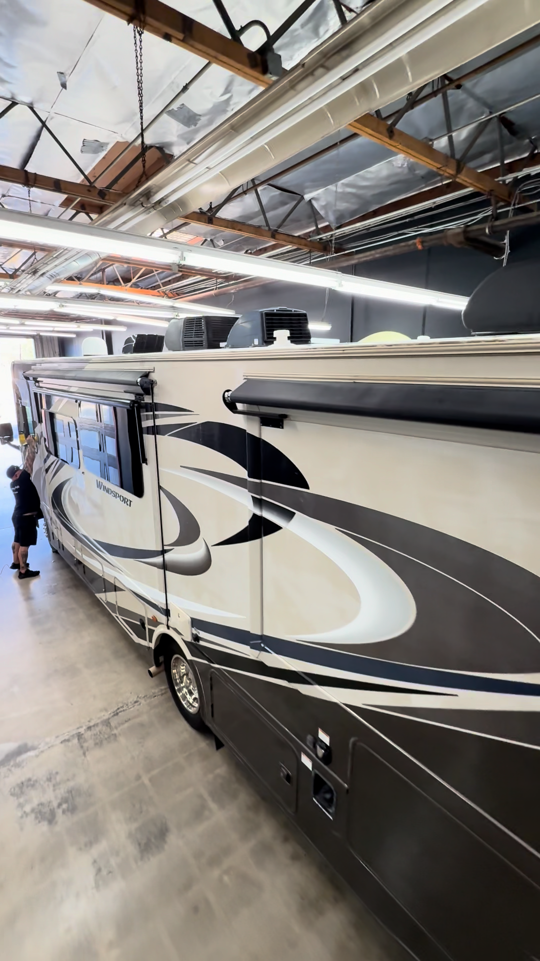Large white and gray RV with black swirls parked indoors in a warehouse-like garage