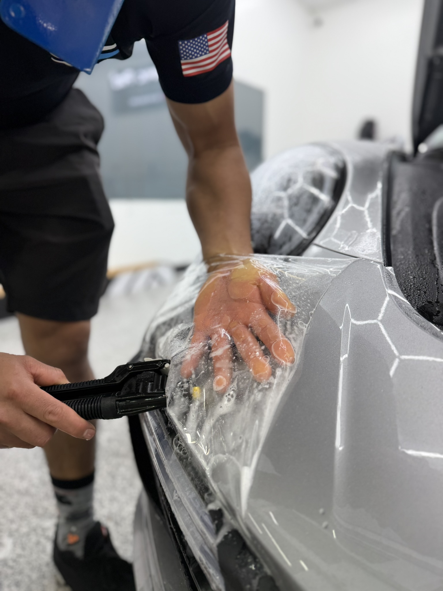 Person washing a silver sports car with soap and a hose in a garage