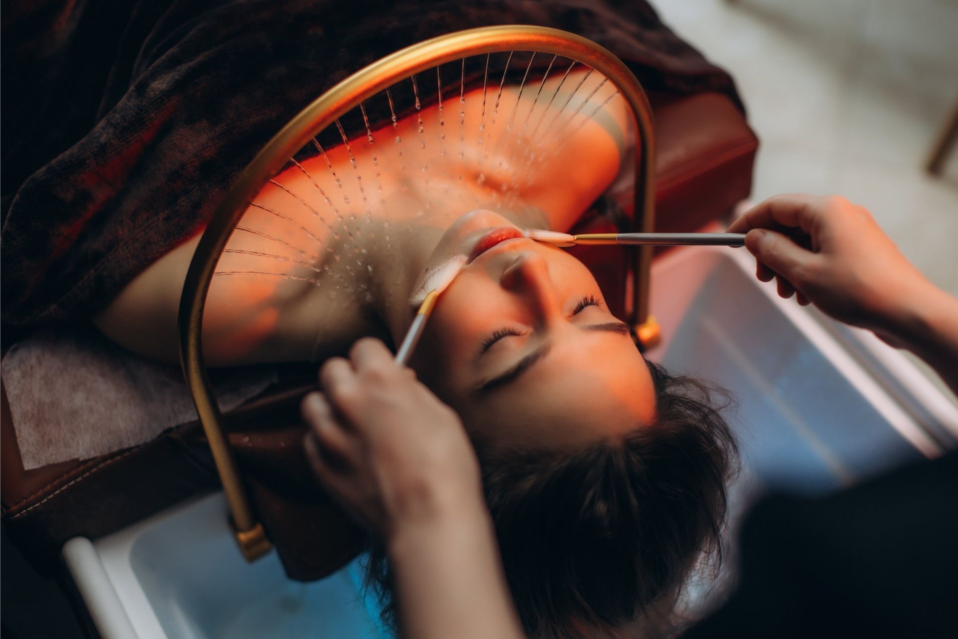 Woman receiving facial treatment, with light therapy and esthetician applying products.