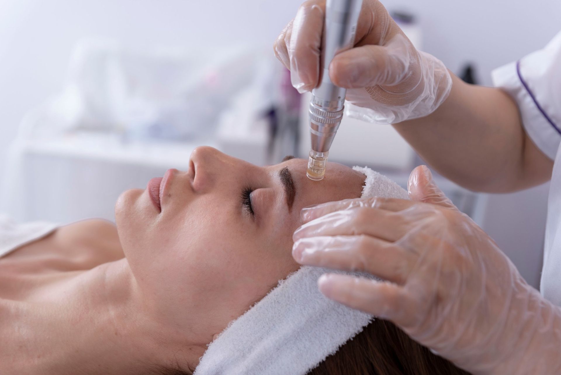 Person receiving a facial treatment. A gloved hand uses a device on the person's forehead, in a medical setting.