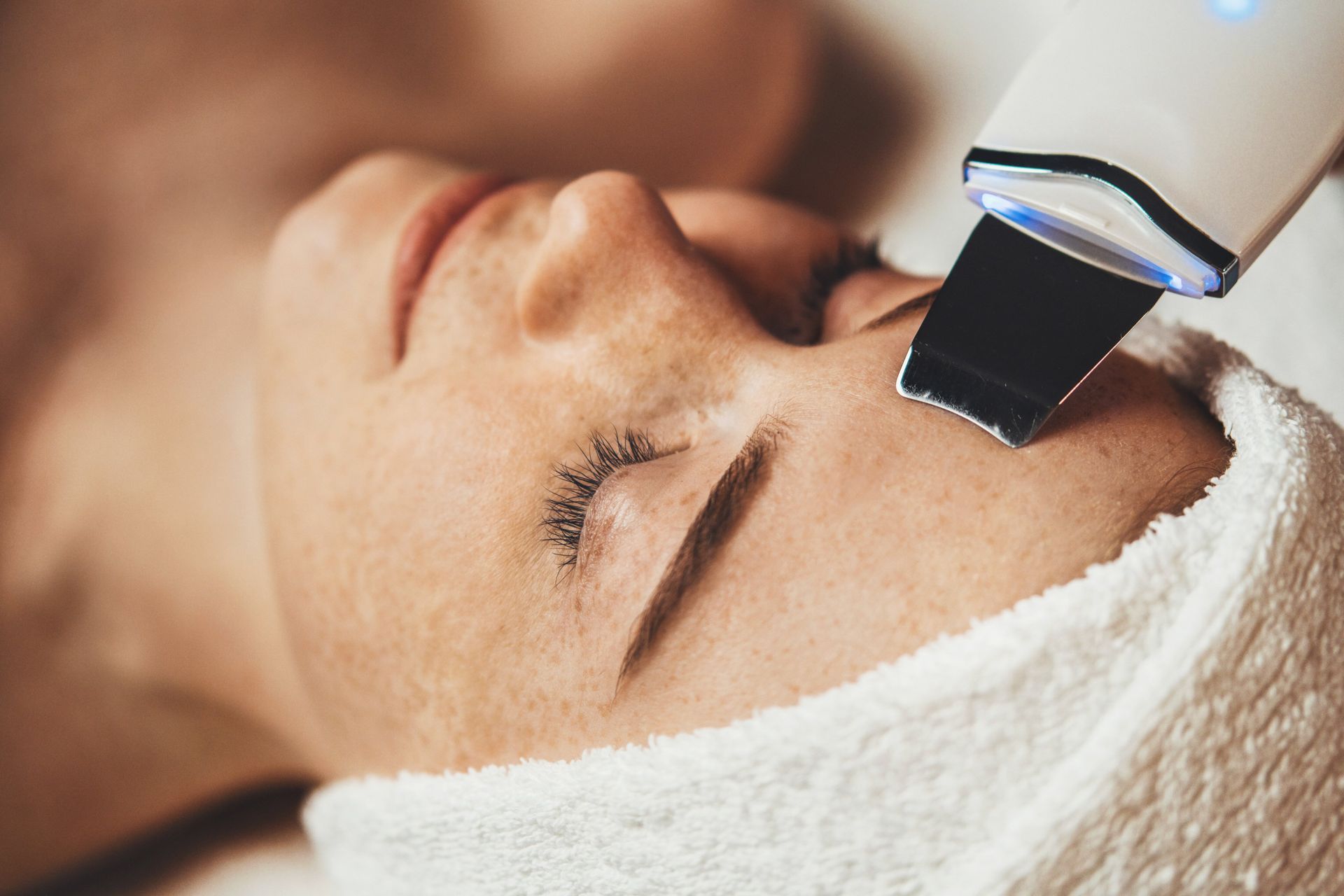 Woman receiving facial exfoliation with a spatula tool, white towel, close-up.