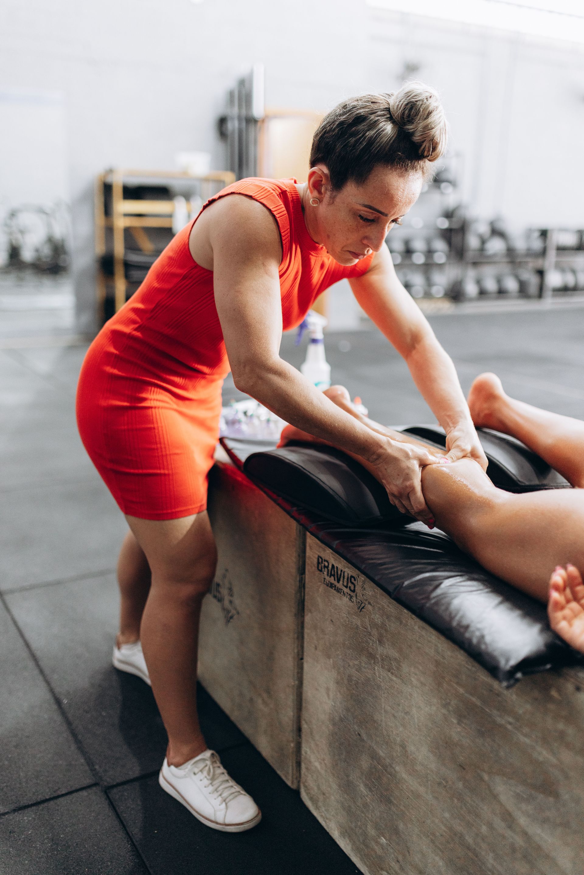 Trainer stretching a person on a gym table, with weights blurred in the background.