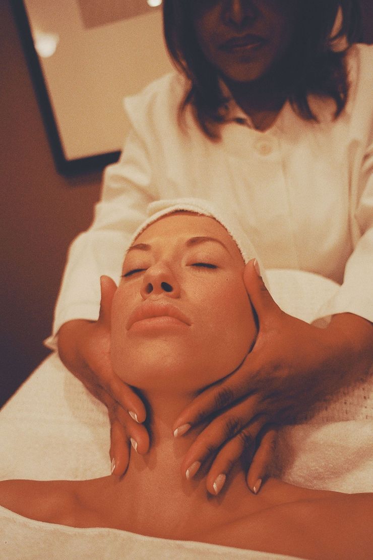 Spa therapist giving a facial massage to a reclining client in a treatment room