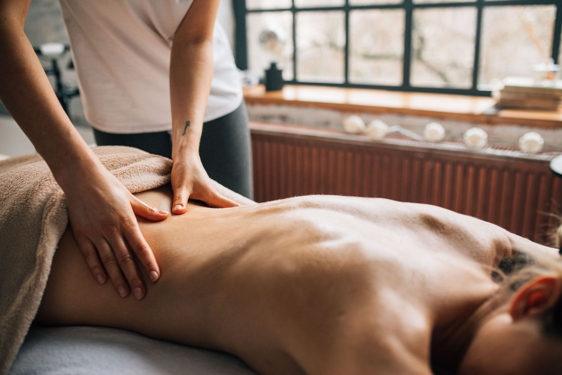 Massage therapist giving a back massage to a client on a table in a bright room