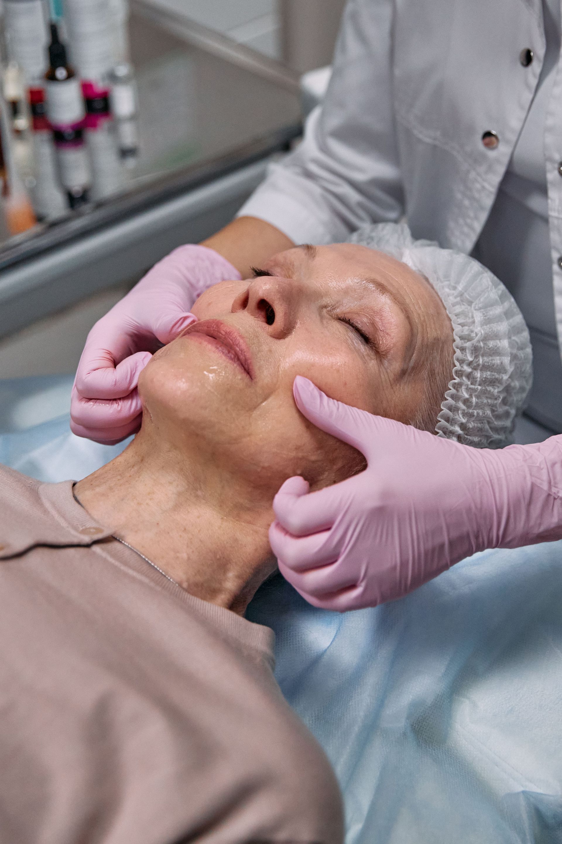 Gloved hands massage an older patient’s face in a clinical treatment room