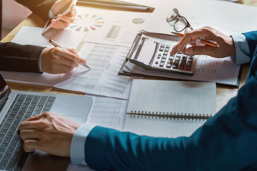 Two people are sitting at a table with a laptop and a calculator.