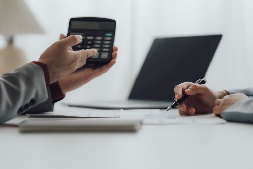 A man is holding a calculator in his hand while a woman is writing on a piece of paper.