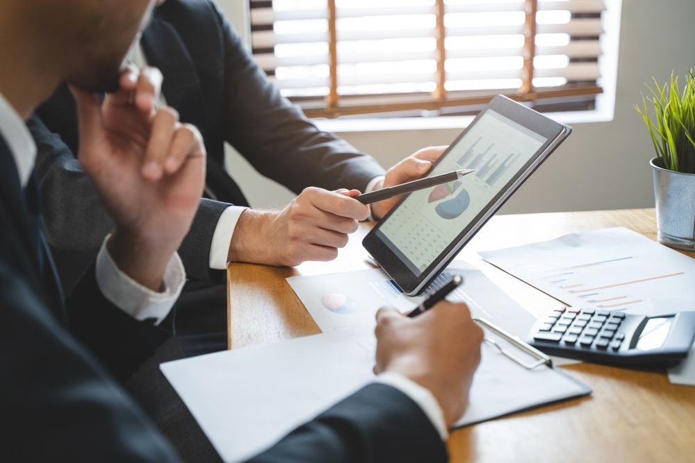 Two men are sitting at a table looking at a tablet.