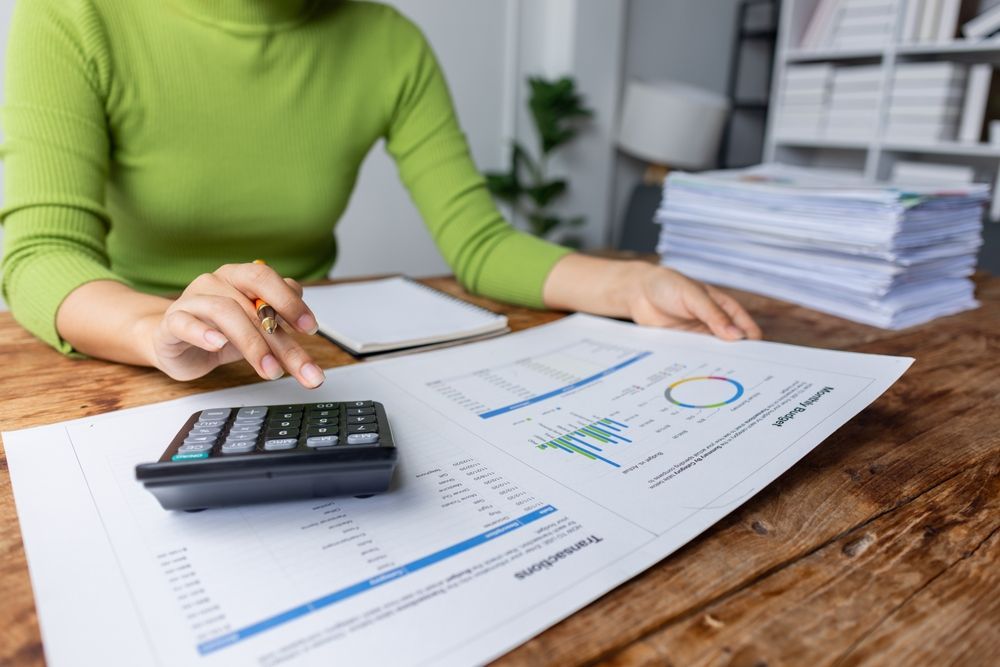A woman is sitting at a table with a calculator and a tablet.
