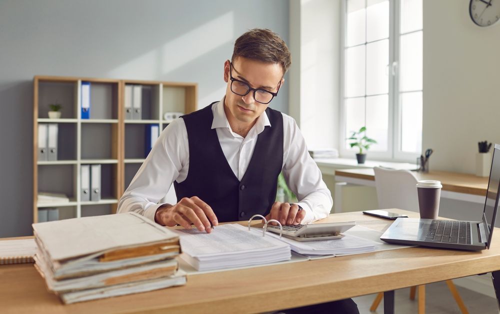 A man is sitting at a desk in an office using a calculator.