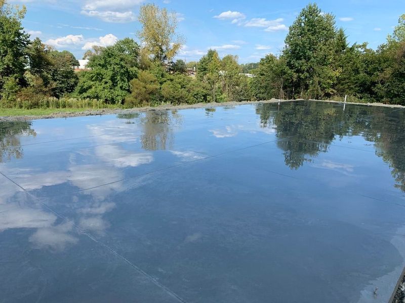 A wide expanse of wet concrete reflects the blue sky and surrounding trees like a mirror.