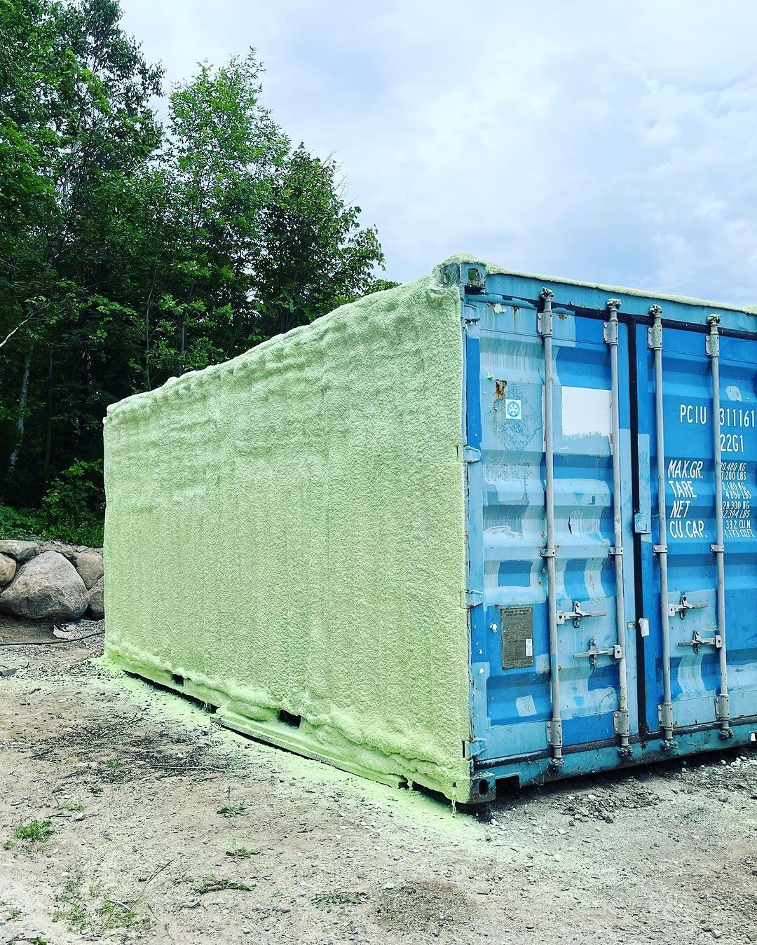 A blue shipping container is covered in green foam.