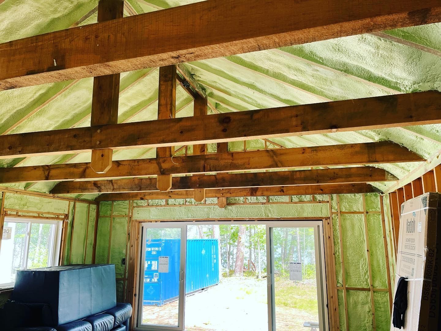 Interior view of a building with exposed wooden beams and green spray foam insulation on the walls and ceiling.