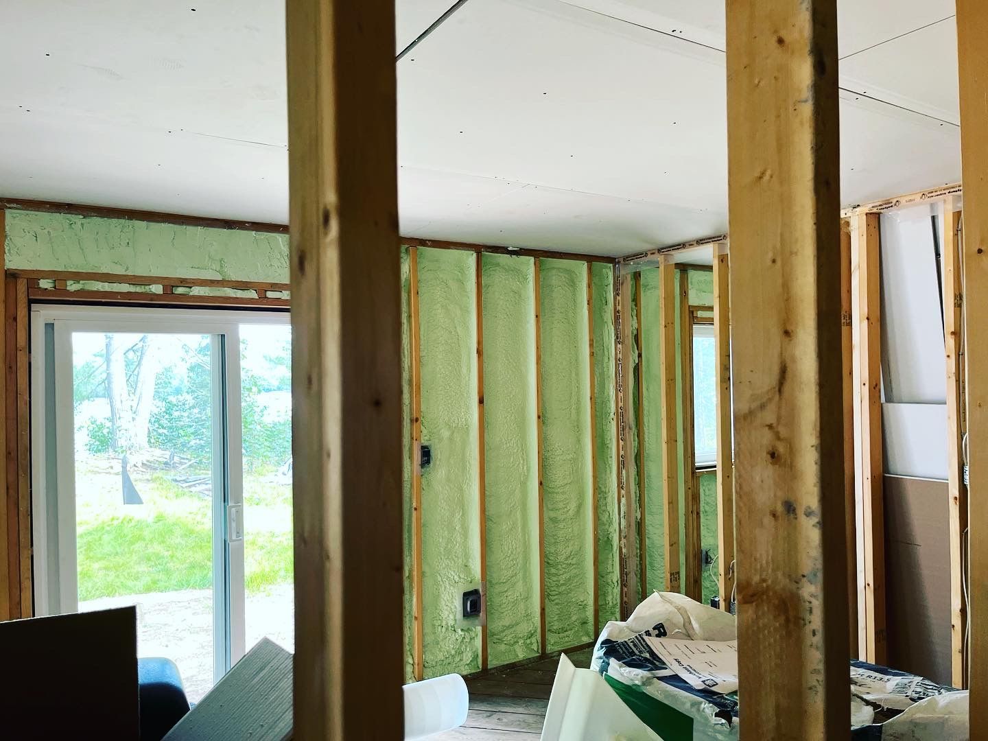 Interior under renovation with green foam insulation between wall studs and window facing outside.