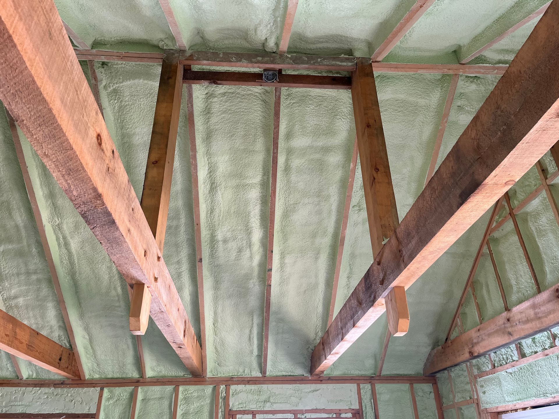 View from below of a ceiling with exposed wood beams and light green spray foam insulation.