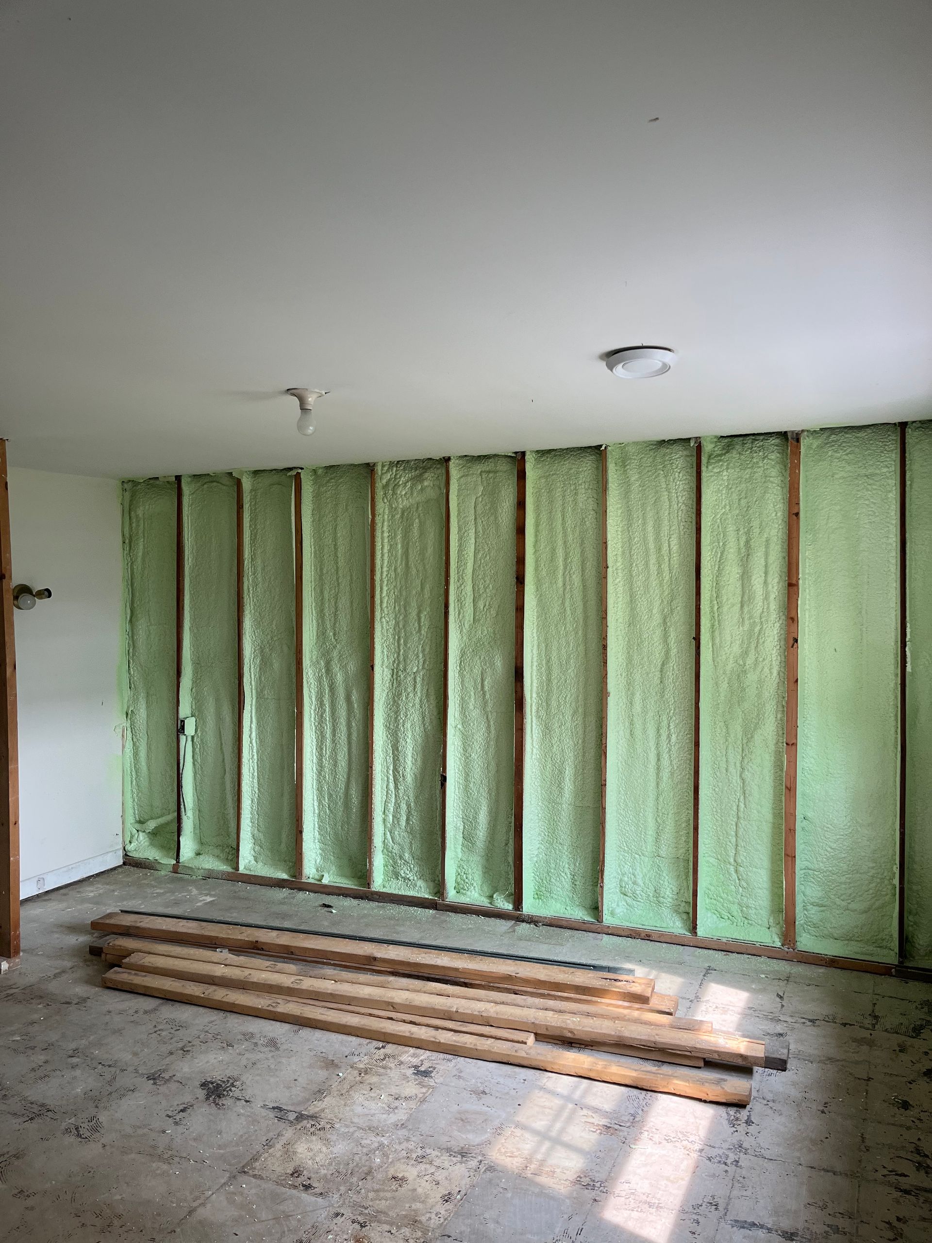 A room with green insulation on the walls and a pile of wood on the floor.