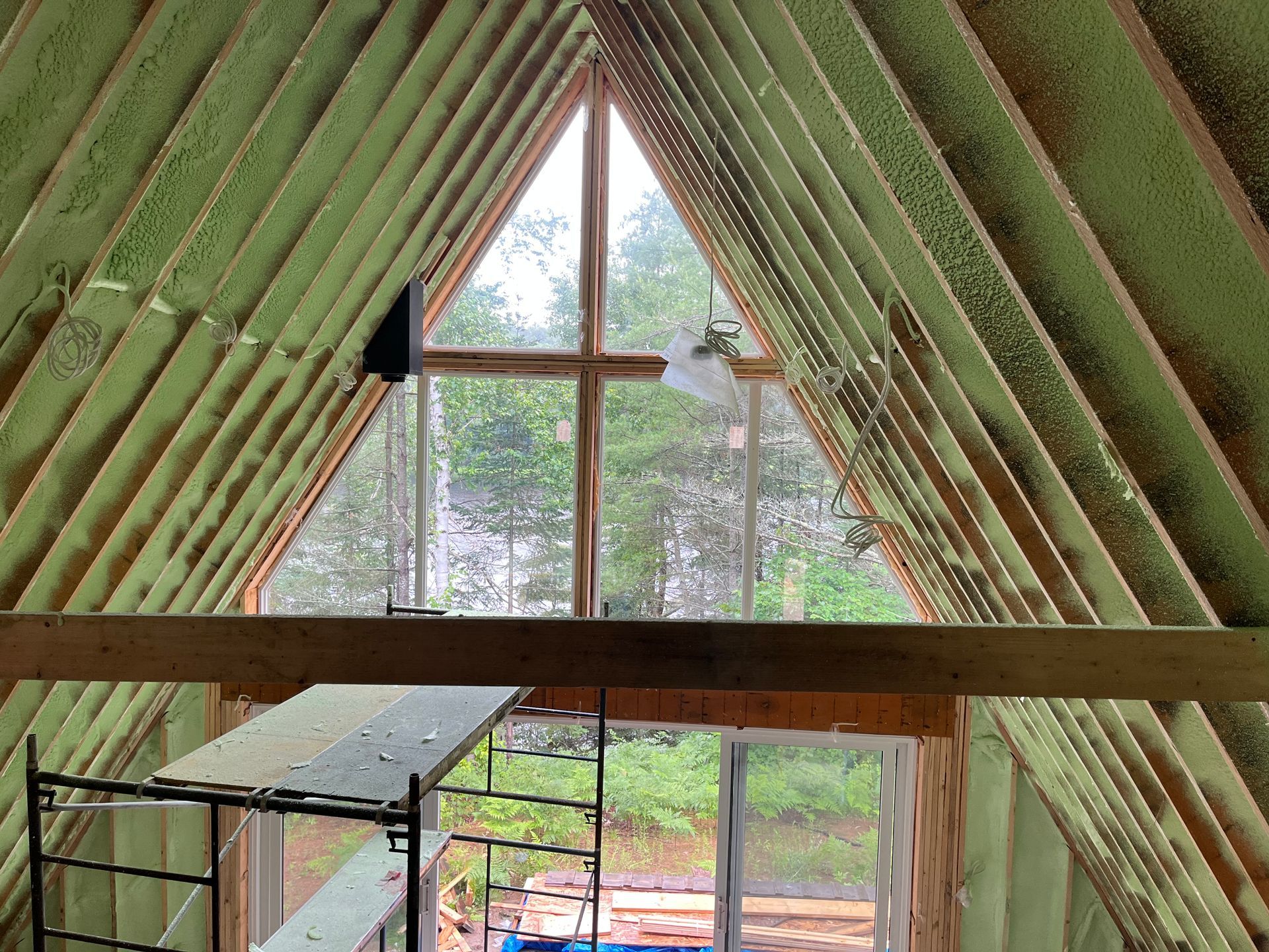 Interior view of a triangular roof with spray foam insulation. A window and door frame the outside view.