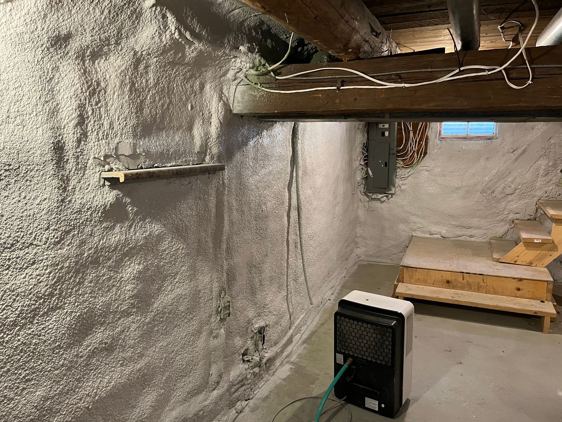 Basement wall with spray foam insulation, power outlet, stairs, and a space heater.