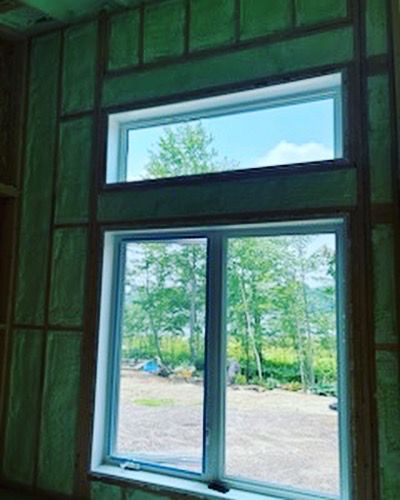 A window in a room with green insulation and a view of trees.