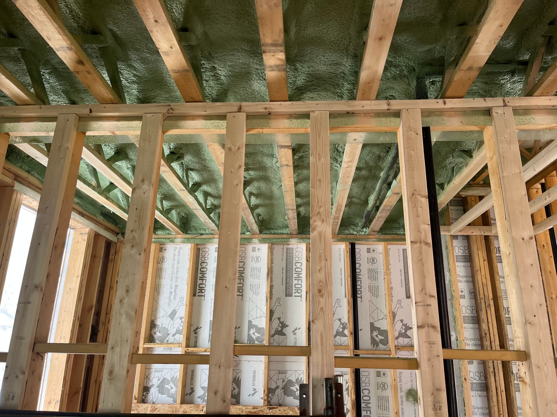 Interior of a room under construction with green thermal insulation, wooden studs, window, and concrete floor.