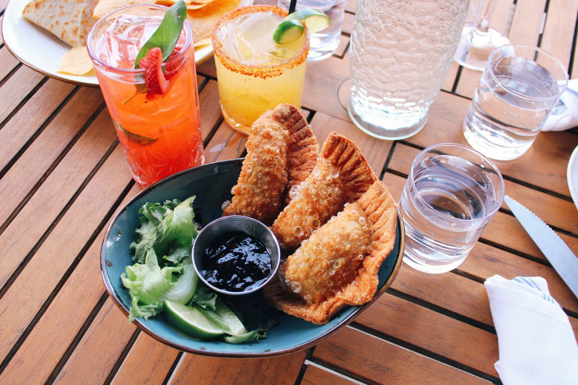 Plated fried fish with broccoli and dipping sauce on a wooden table with colorful drinks