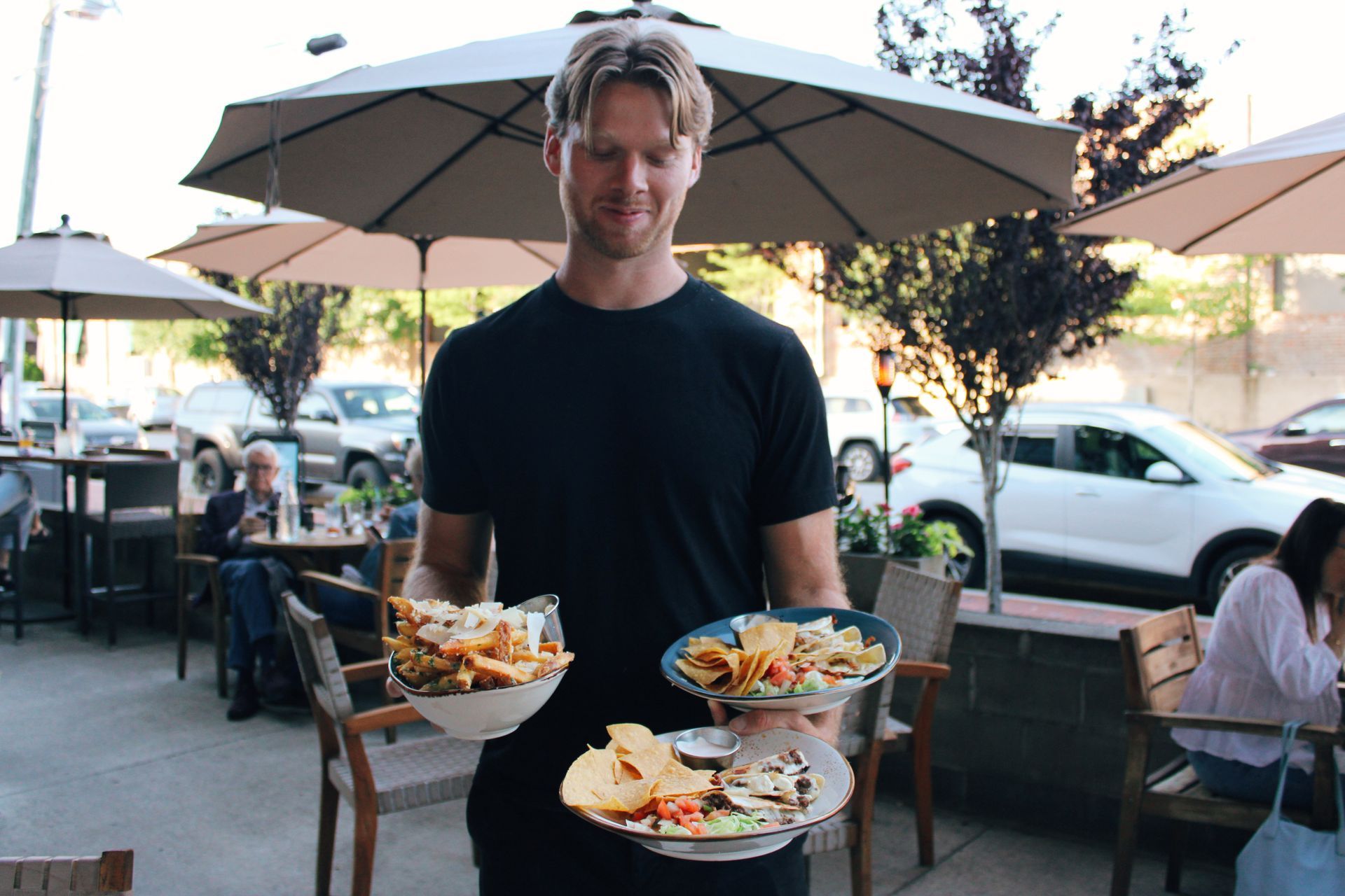 Server carrying three plates of food at an outdoor restaurant patio