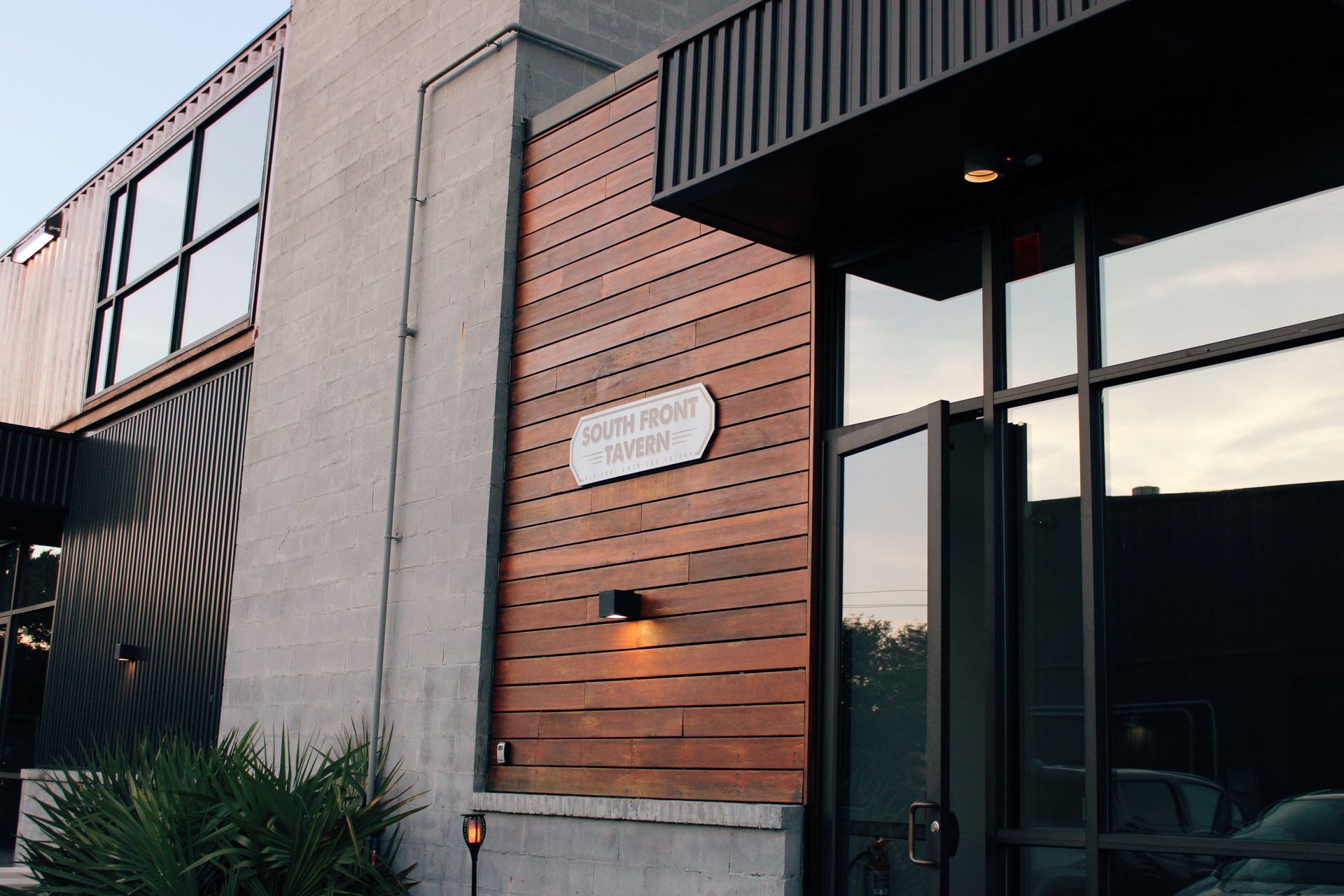 Modern building exterior with wood siding, large windows, and a glass entrance at dusk