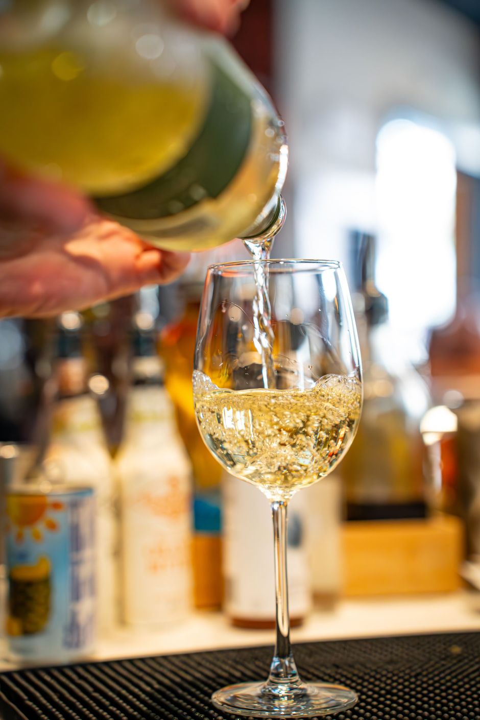 Wine being poured into a glass at a bar, with bottles blurred in the background.