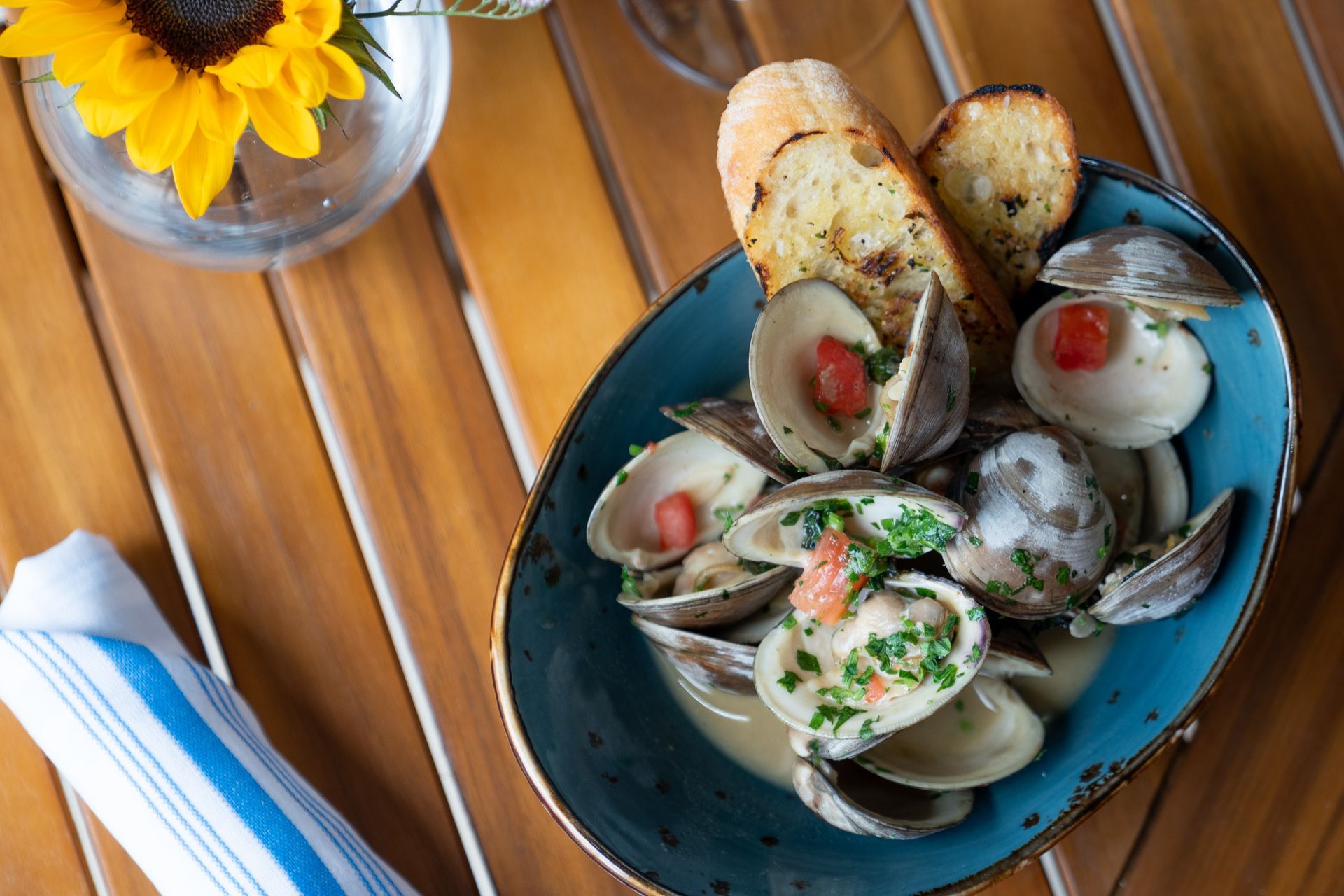 Clam dish with toasted bread on a blue plate beside a sunflower centerpiece on a wooden table