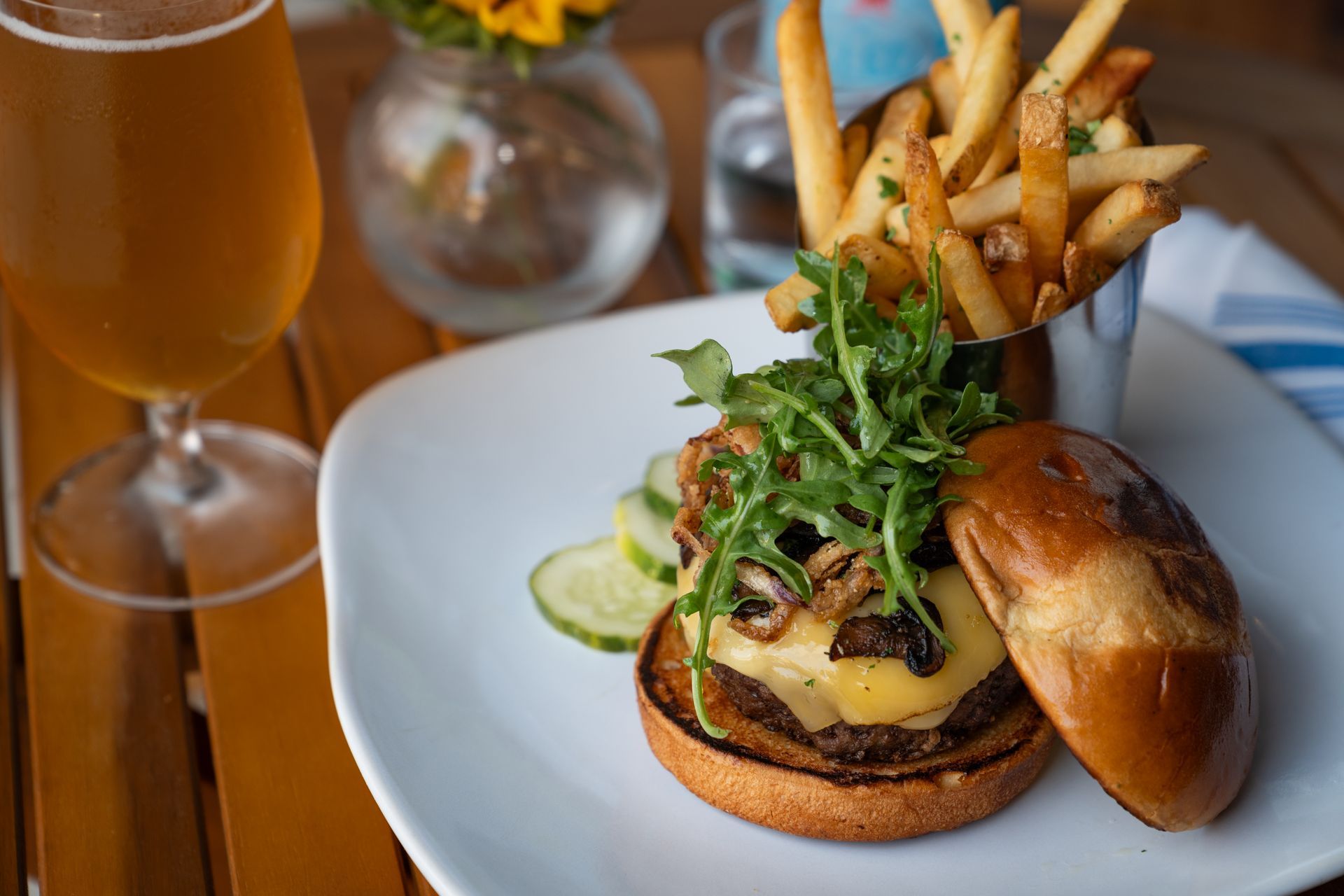 Burger with fries and lime on a white plate beside a glass of beer in a restaurant setting