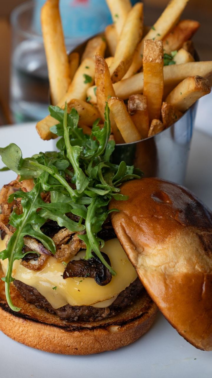 Cheeseburger with arugula and fries in a metal cup