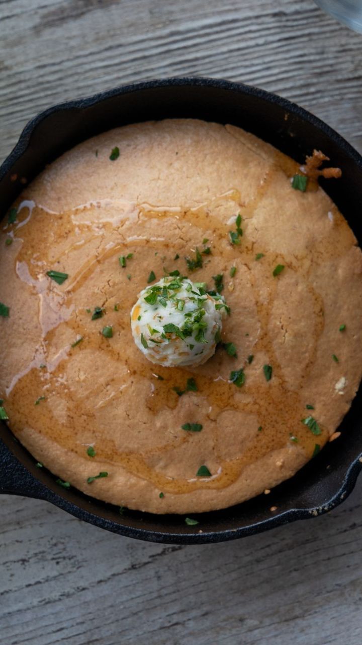 Creamy orange soup in a black bowl, topped with a dollop of herb butter and chopped herbs.