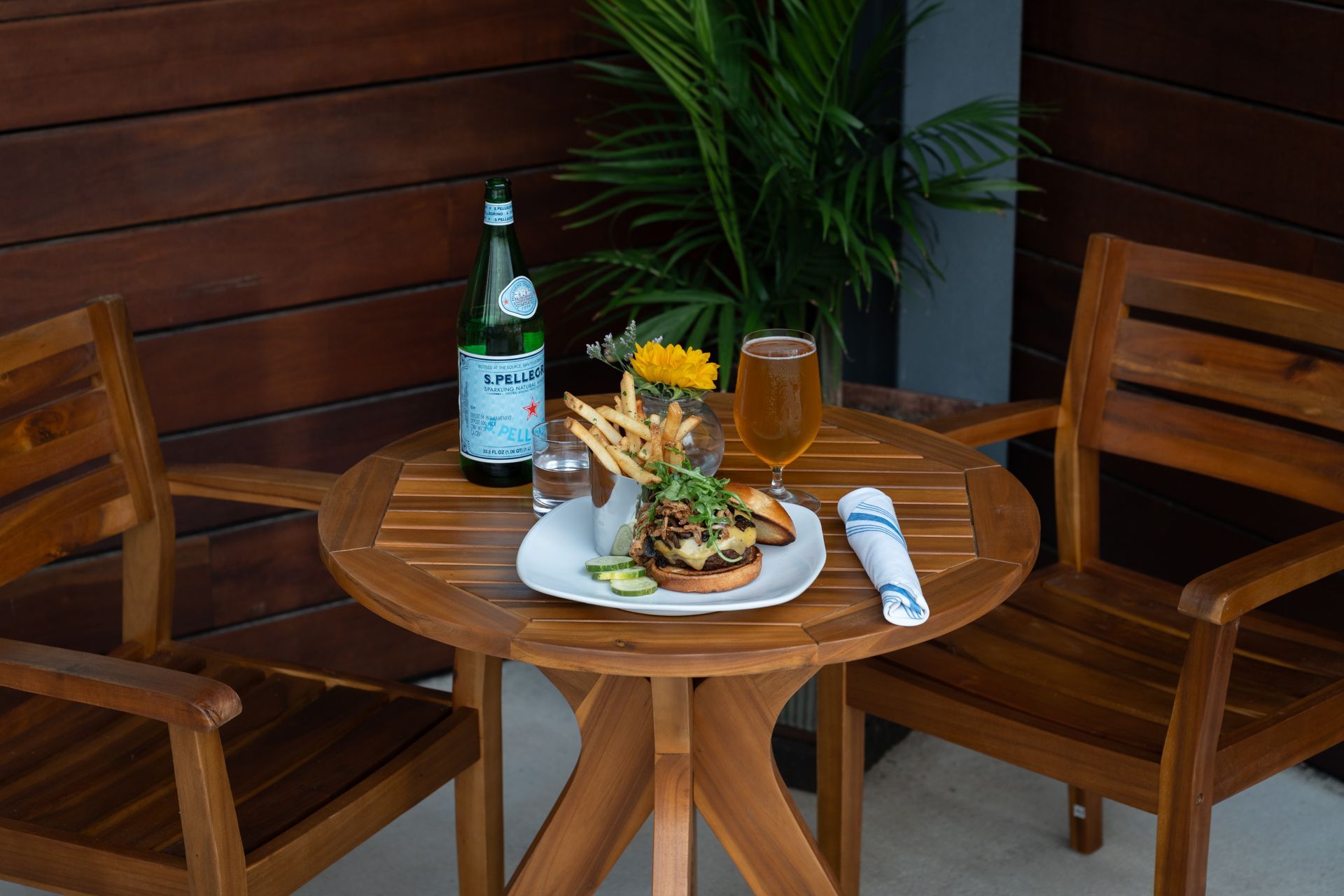 Outdoor wooden table with a plated meal, drink, beer bottle, and two chairs on a patio