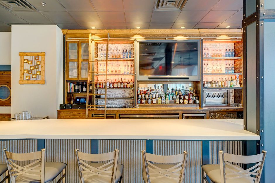 Modern bar with white counter, shelves of bottles, and wicker chairs in a stylish interior.