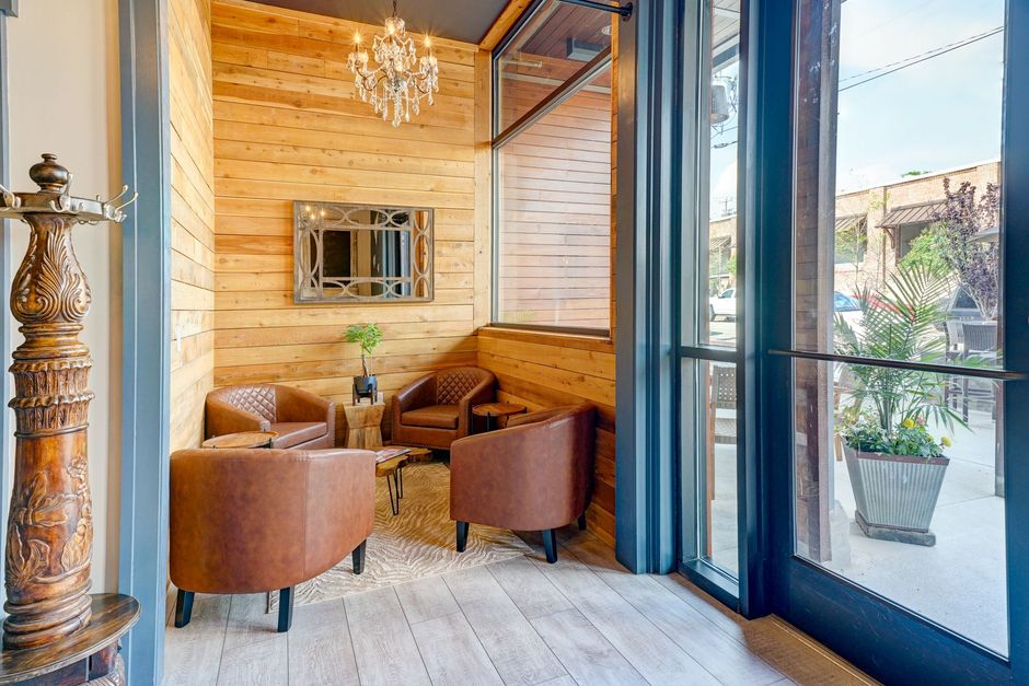 Cozy lounge with tan chairs, chandelier, wall mirror, and large window overlooking greenery