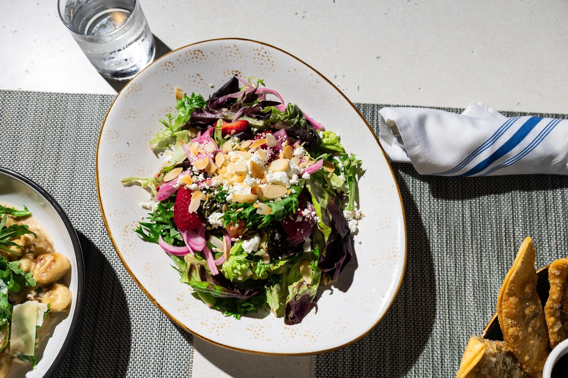 Fresh salad with greens, beets, and cheese on a table beside a glass of water and breadsticks.
