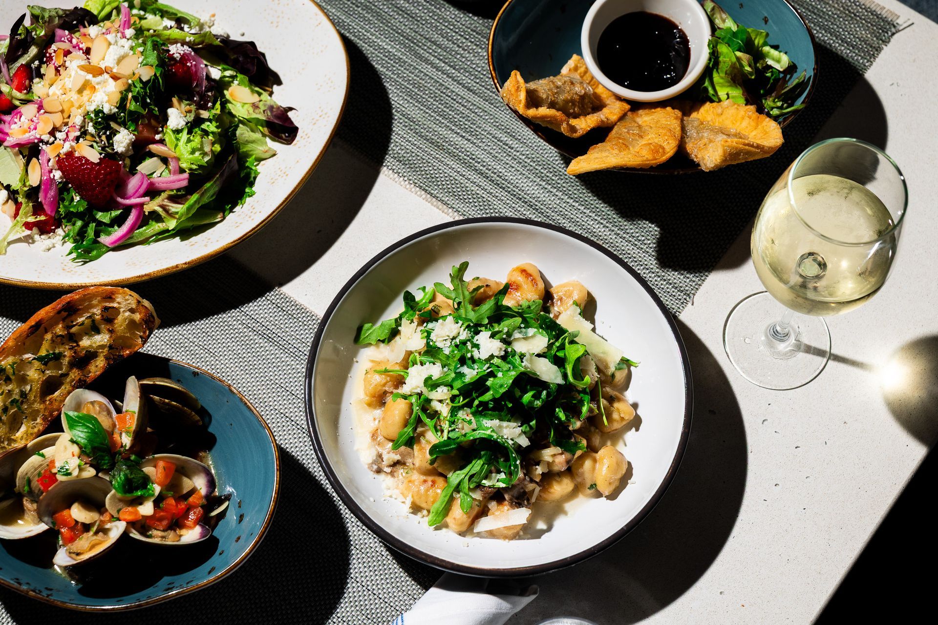 Overhead view of a table with salads, dip, bread, and a glass of white wine