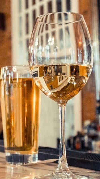 A wine glass and a tall beer glass filled with amber drinks on a bar counter