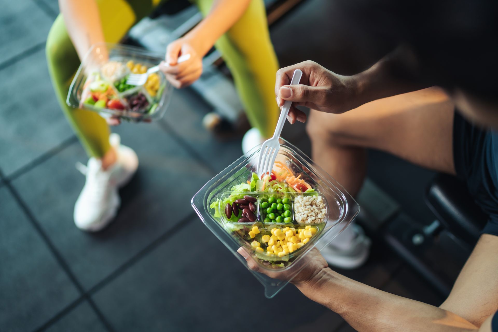 A man and a woman are eating salads in a gym.