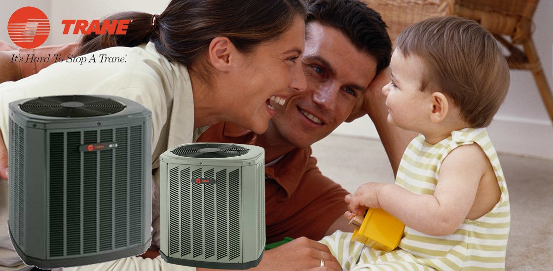 Family smiles, with a baby, near two Trane air conditioning units, suggesting home comfort and safety.
