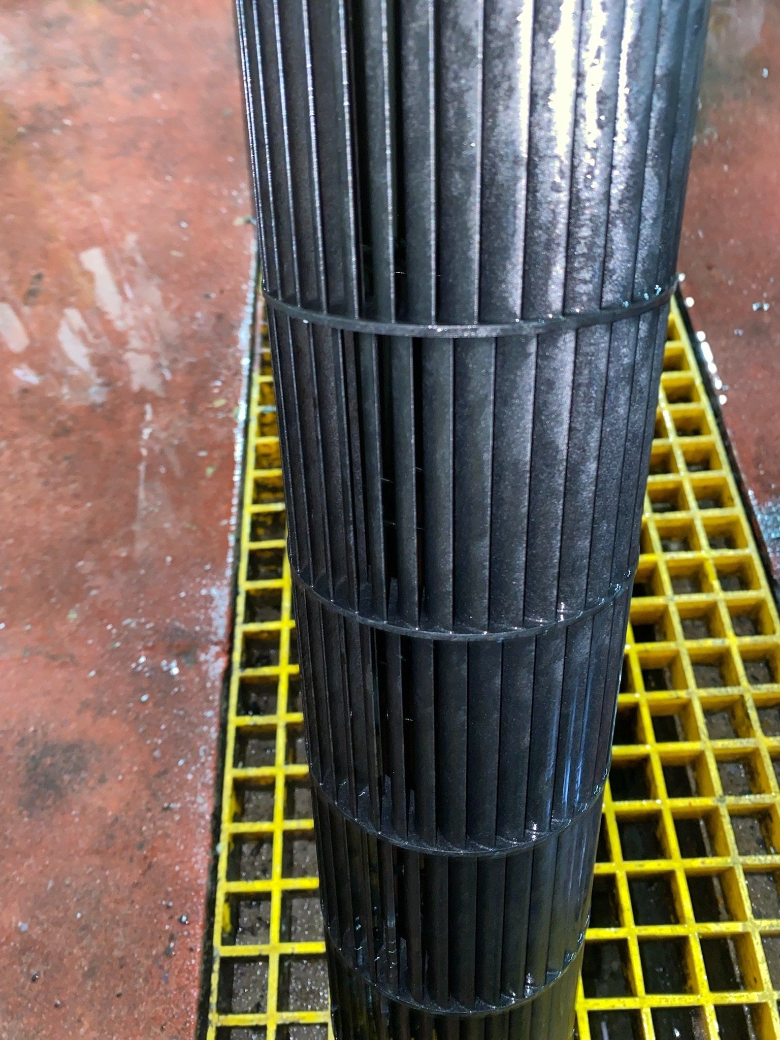 A cylindrical, black air filter on a yellow grated surface, covered in dust or residue.