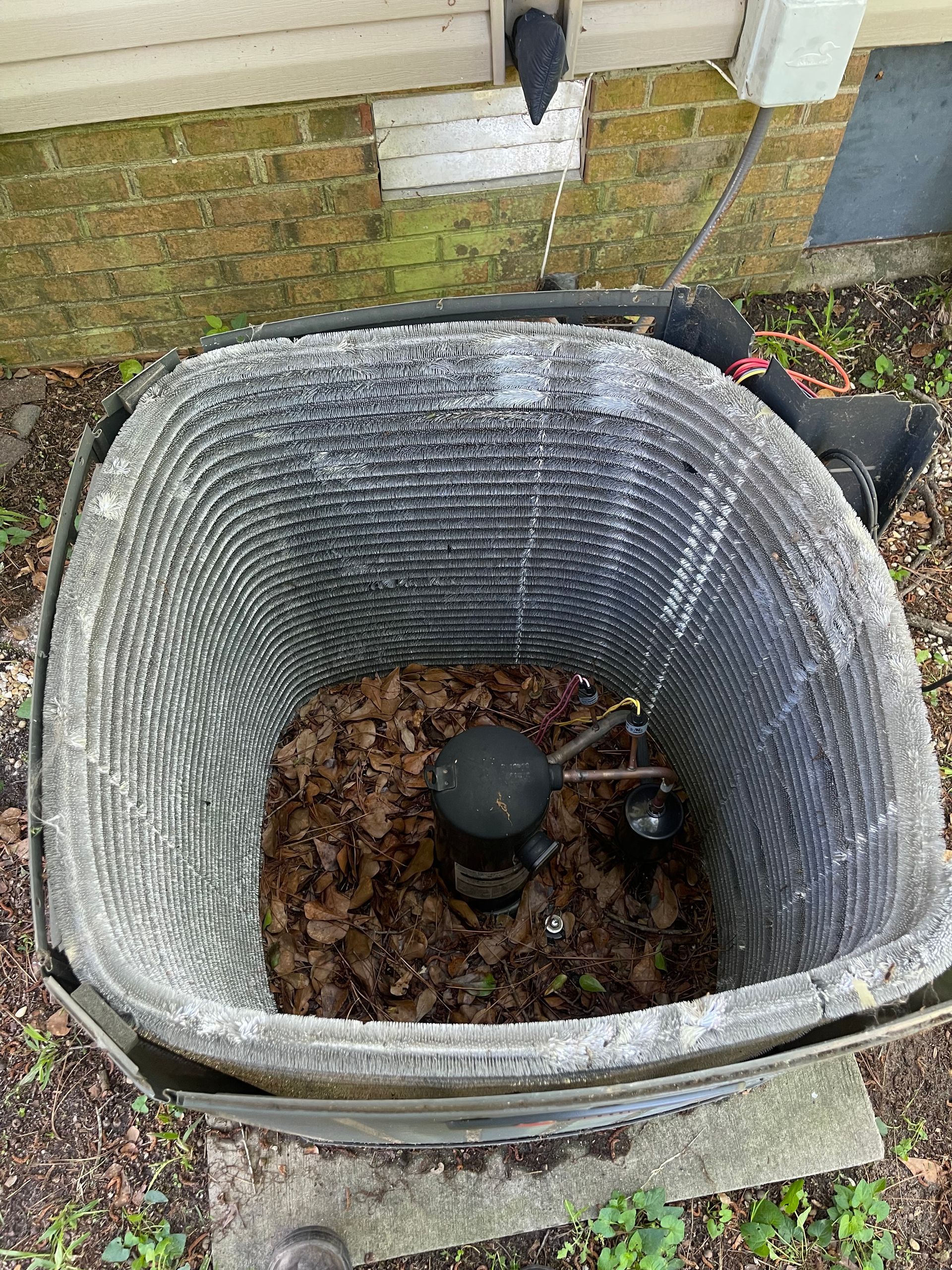 Outdoor air conditioning unit with debris, against a brick wall.