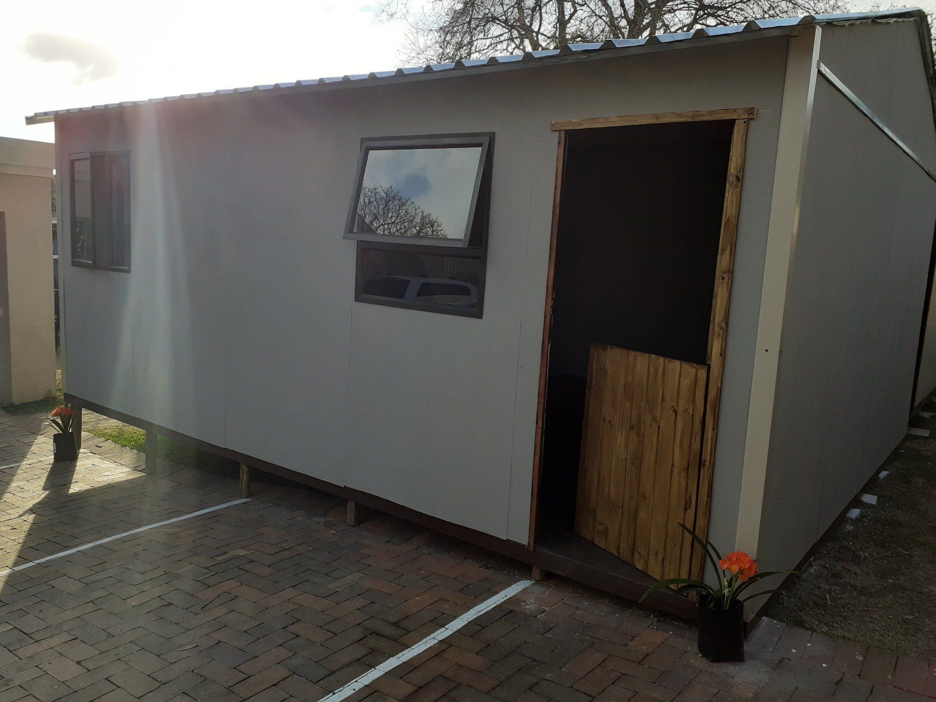 A small white building with a wooden door and window is in a parking lot.