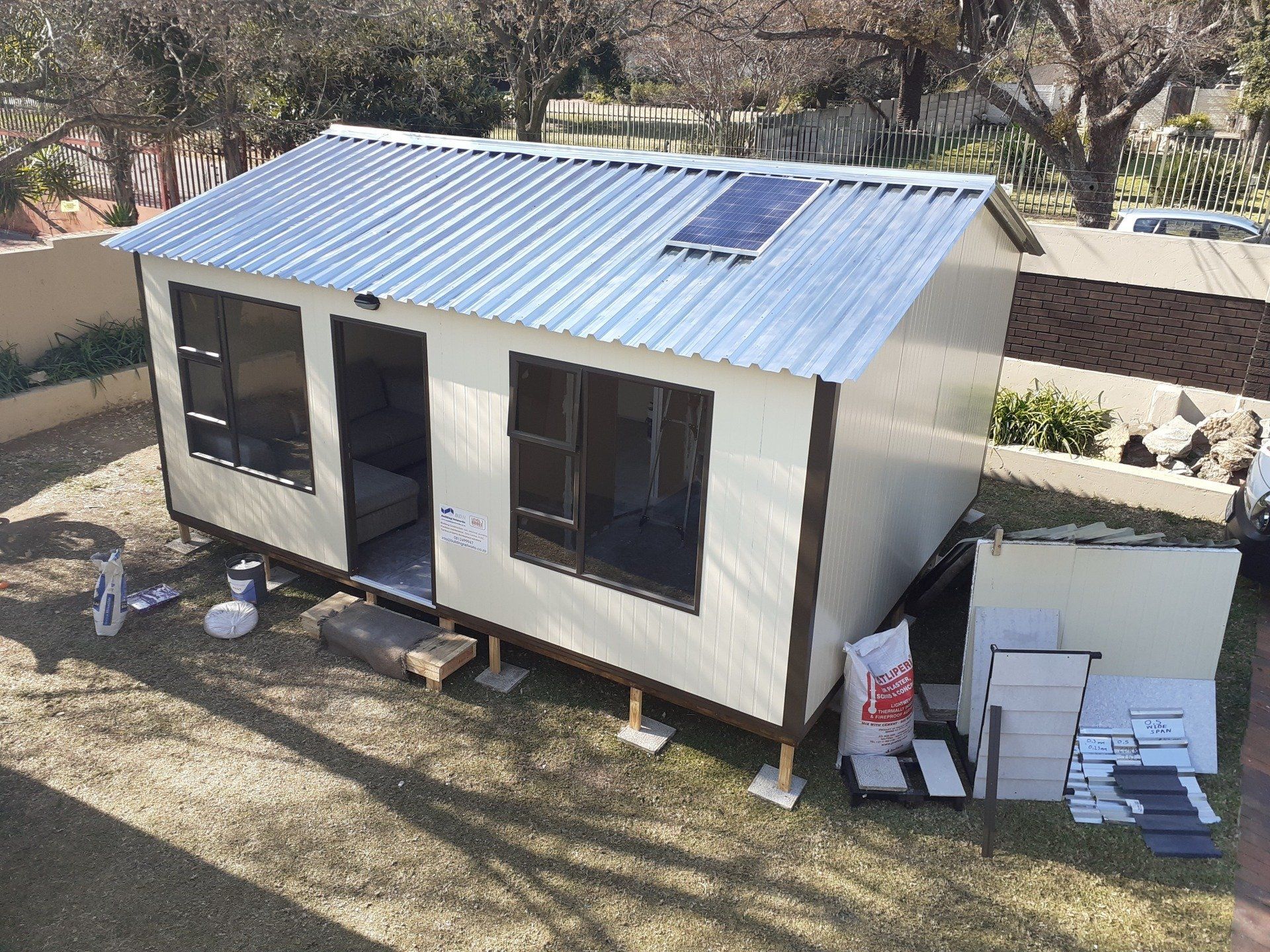 A small house with a solar panel on the roof is being built in a backyard.