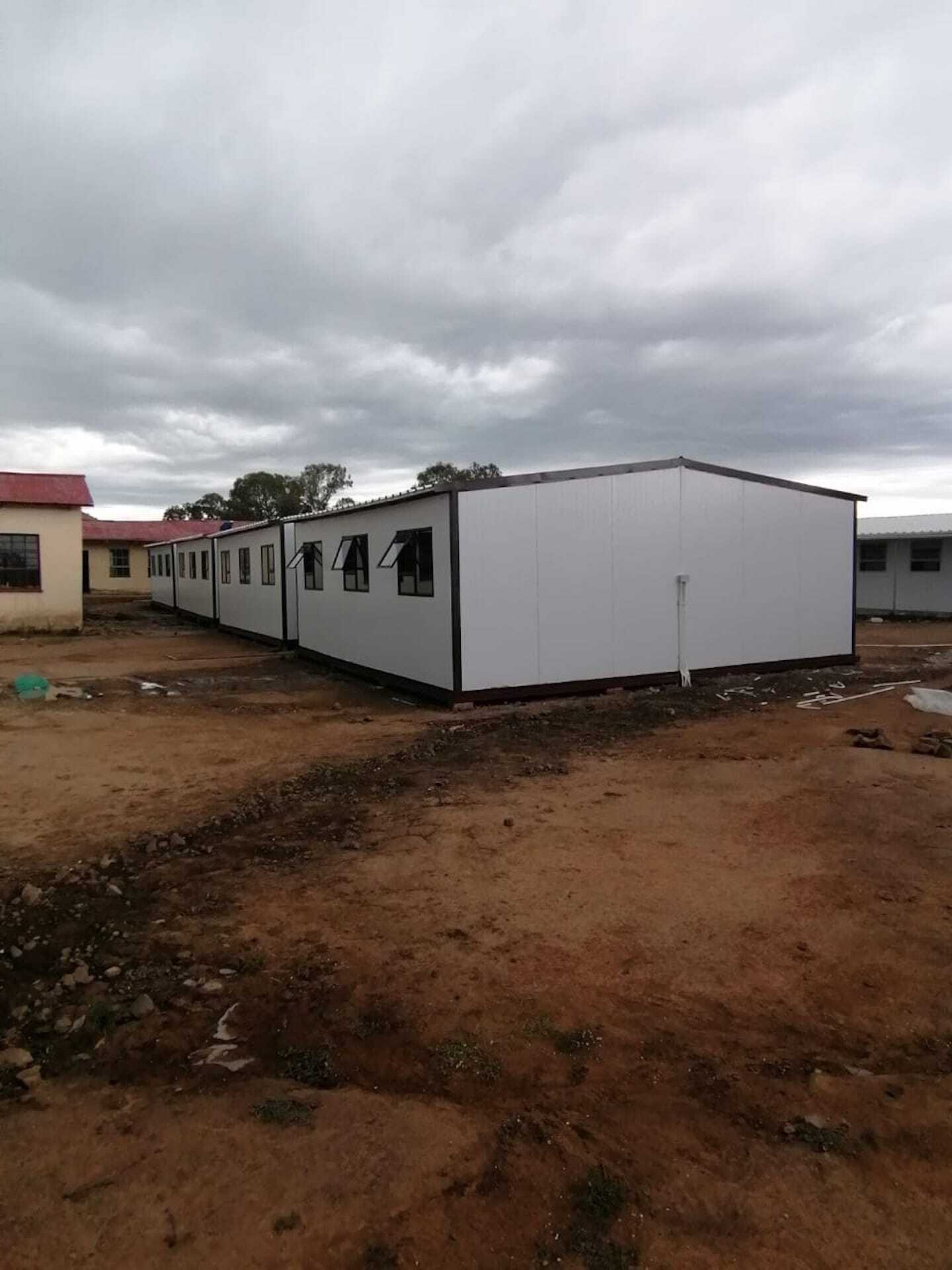 A row of buildings in a dirt field with a cloudy sky in the background.